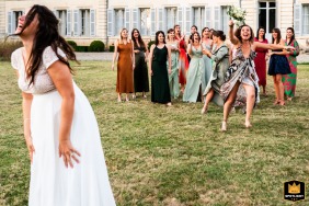 Lancio del bouquet nuziale nel giardino di Château Saint Denis a Lot et Garonne, in Francia. Un gruppo di donne guarda con impazienza mentre una fortunata scappa con gioia con il bouquet catturato.